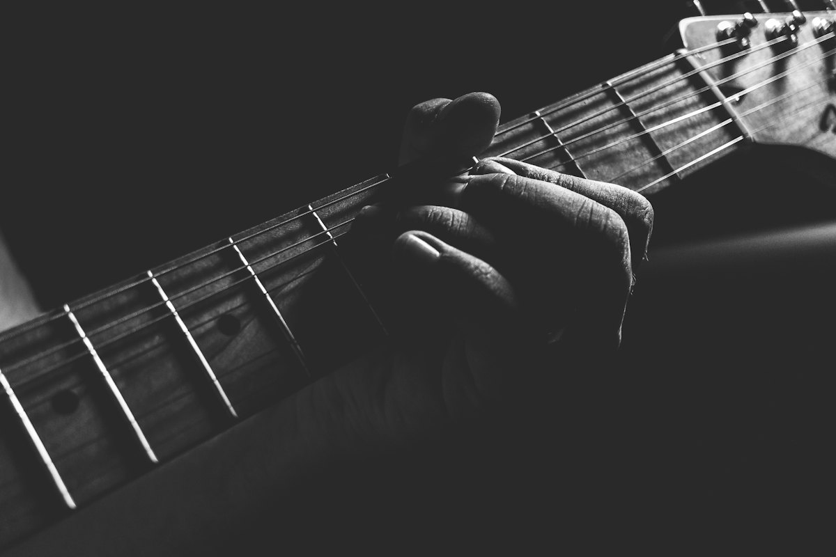 Black and white close-up of fingers pressing the strings on a guitar fretboard
