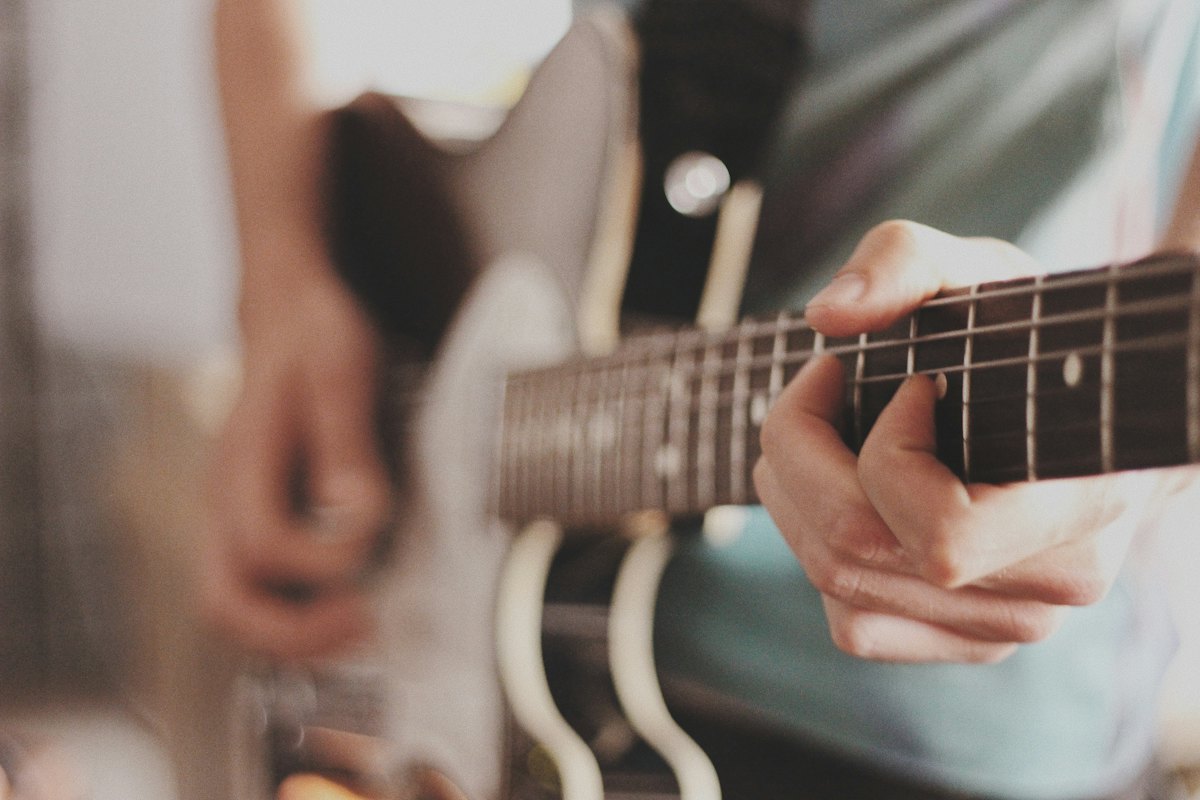 Close-up of a guitarist&rsquo;s hands on the neck of a cream electric guitar