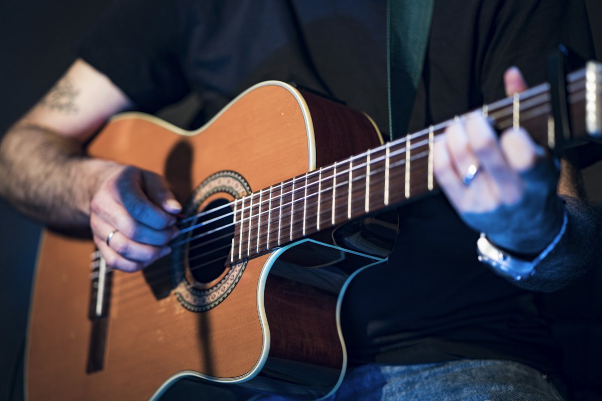Man playing a cutaway acoustic guitar against a dark background