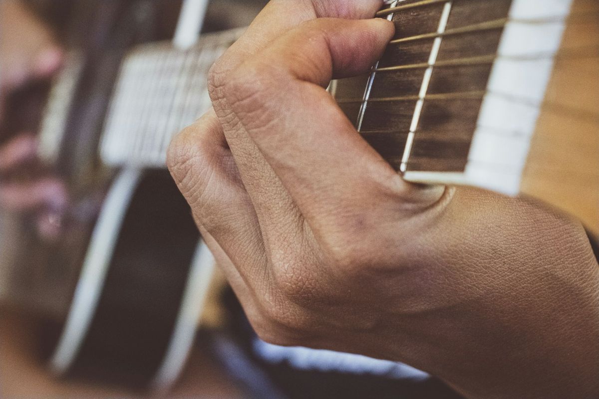 Close-up of a hand fretting a chord on the neck of an acoustic guitar