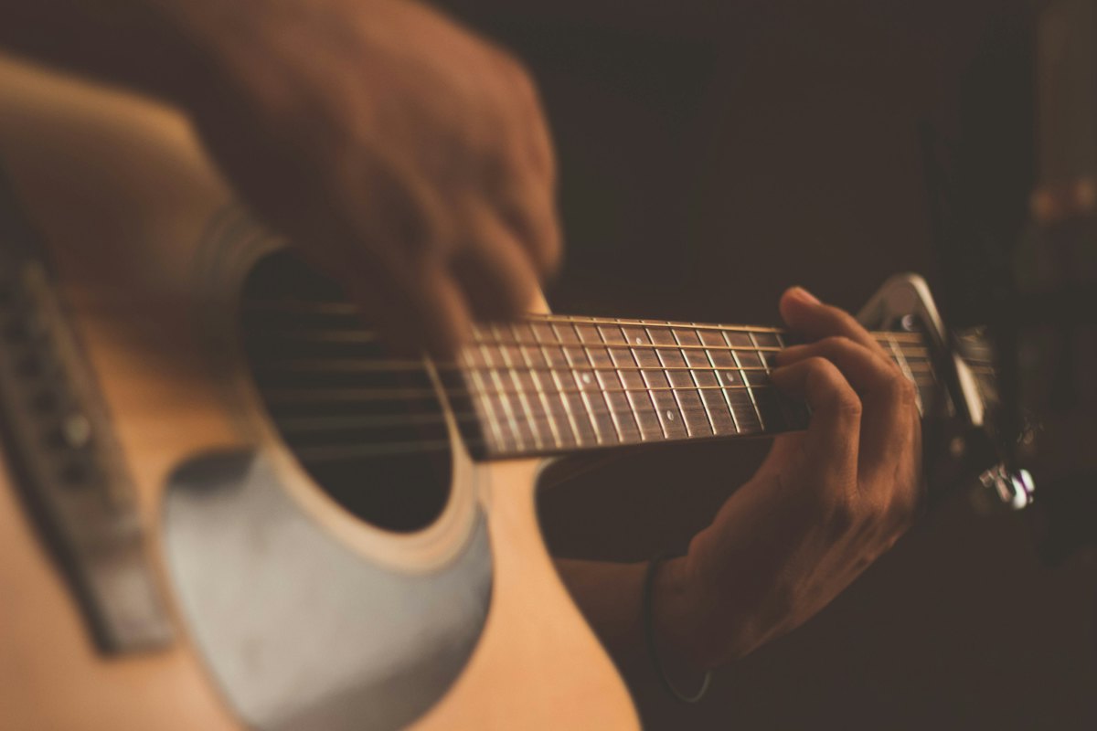 Close-up of a hand fretting a chord on the neck of an acoustic guitar in warm light