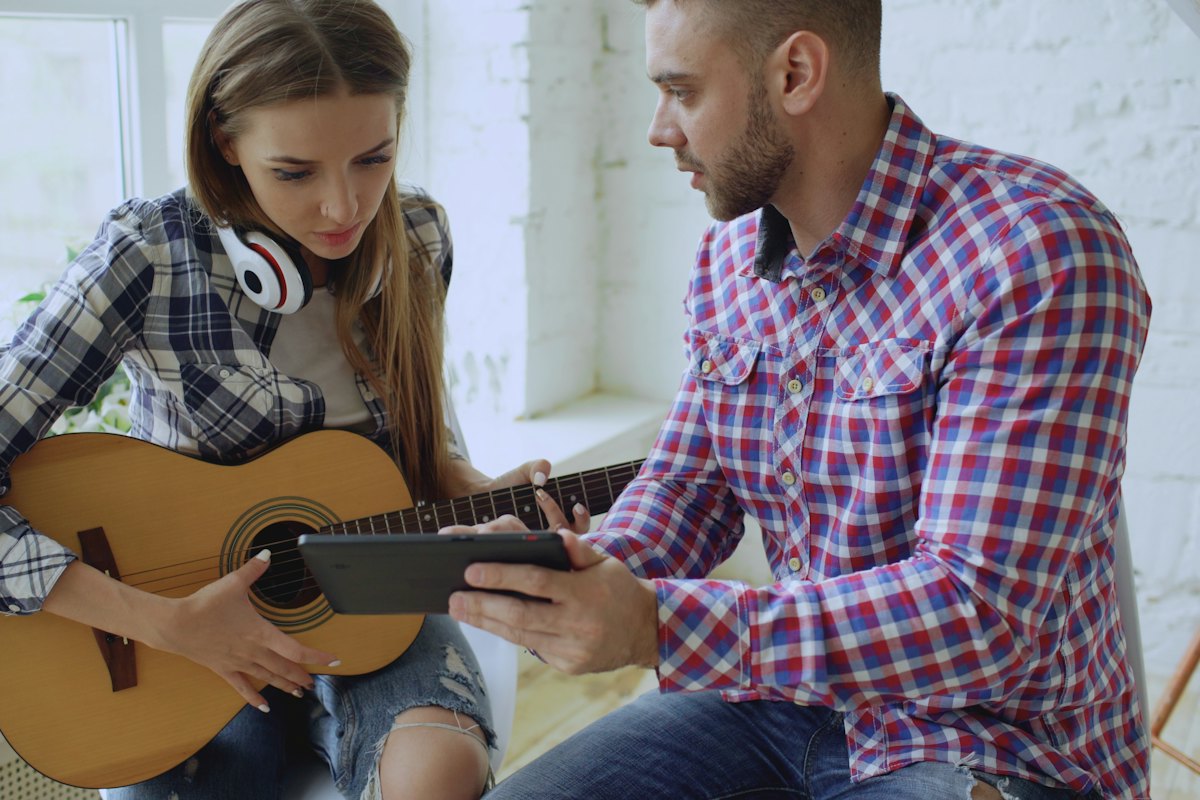 Guitar teacher showing a lesson on a tablet to a teenage student holding an acoustic guitar