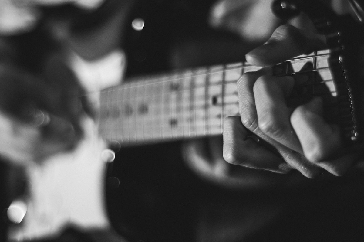 Black and white close-up of a hand fretting a chord on an electric guitar