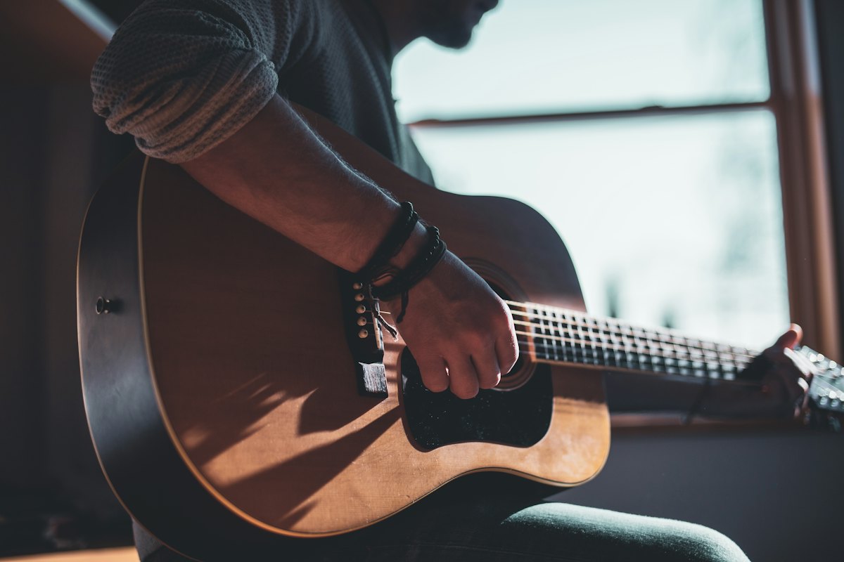 Man playing an acoustic guitar beside a bright window